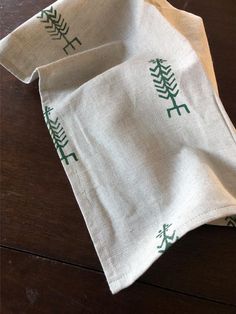 two linen napkins with trees on them sitting on a wooden table next to each other