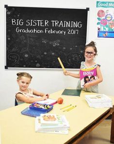 two children sitting at a table with books and pencils in front of a blackboard