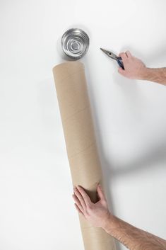 a man holding a roll of toilet paper with a can on the floor next to it