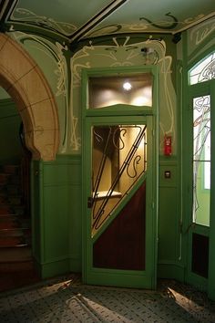 an open door leading to a stairway in a green room with ornate designs on the walls