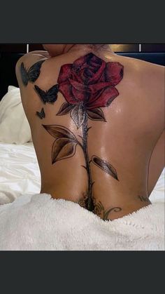 the back of a woman's body with tattoos on it and a rose tattoo