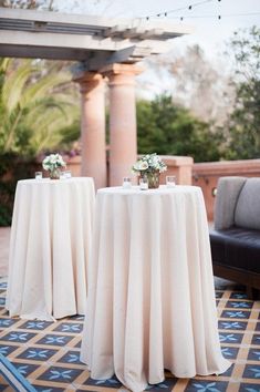 two tables covered with white tablecloths sitting on top of a tiled floor next to couches