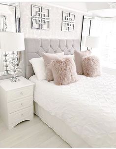 a white bed topped with pillows next to a night stand and dresser under a mirror