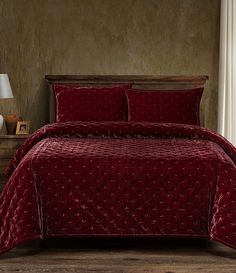 a bed with red comforter and pillows in a room next to a lamp on a table