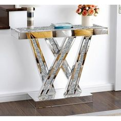 a mirrored console table with gold and silver trimmings on the legs, in front of a white wall