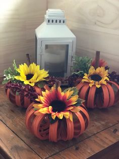 three pumpkins with sunflowers in them sitting on a table next to a lantern