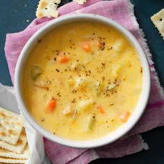 a white bowl filled with soup next to crackers on top of a purple towel