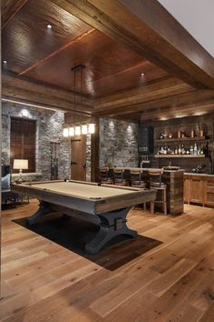 a pool table in the middle of a room with wood flooring and stone walls