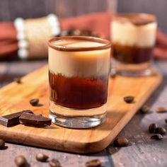 two shot glasses filled with liquid and chocolate on a cutting board surrounded by coffee beans