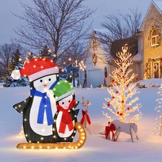 christmas decorations in front of a house with snowman and penguin on sleigh