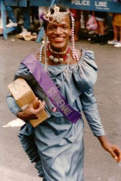 a woman walking down the street with a purple sash around her neck and smiling at the camera