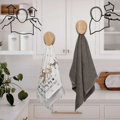 two towels hanging on hooks in a white kitchen with wood utensils and potted plants