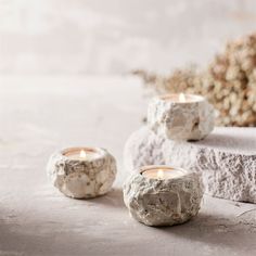 three stone candles sitting on top of each other next to some rocks and flowers in the background