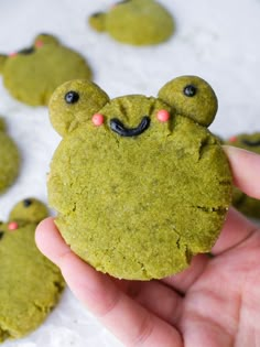 a hand holding up a green cookie with eyes and nose shapes on it's face