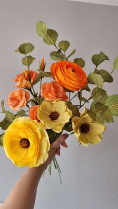 a person holding a bouquet of flowers in their hand, with leaves on the stems