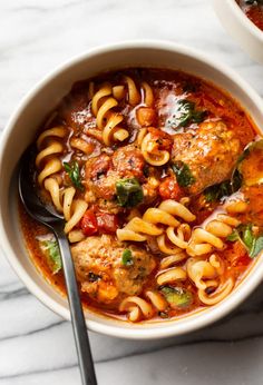 two bowls of pasta with meatballs and tomato sauce on the side, next to a spoon