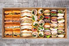 a box filled with lots of different types of sandwiches on top of a wooden table