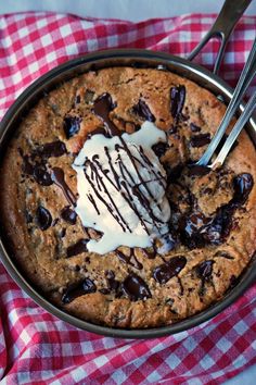 a chocolate chip cookie in a pan with cream drizzled on top and spoons