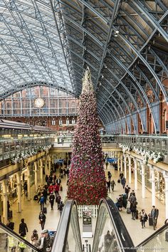 a large christmas tree in the middle of a train station with people walking around it