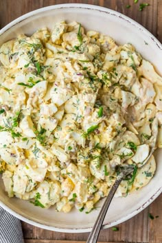 a white bowl filled with chicken salad on top of a wooden table next to a fork