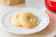 two cookies on a white plate next to a red vase