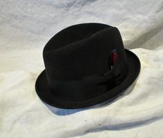 I don't know anything about hats, so what I'm about to describe to you will be a challenge for me. Please bear with me, and if you see egregious errors or can enlighten me, I'd sure appreciate learning from the experts on Etsy! This appears to me to be a men's hat, 100% felted wool in a luxurious black color and the hat is marked "KENWORTH" and "Imperial Finish". It looks like a classic fedora hat, and has that wonderful mid century retro look. Nice ribbon detail and muted red and deep blue feat Classic Fitted Cloche Cap, Classic Fitted Felt Cap, Vintage Fedora Felt Hat, Vintage Fedora Hat, One Size Fits Most, Vintage Short Brim Top Hat, Wood Art Frames, Muted Red, Bear With Me, Red Feather