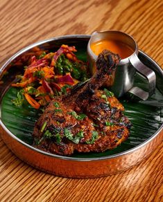 a metal plate topped with meat and veggies next to a cup of sauce