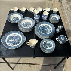 a table topped with blue and white dishes next to a black tablecloth covered sidewalk