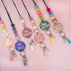 six keychains with different designs and words on them, all hanging from strings