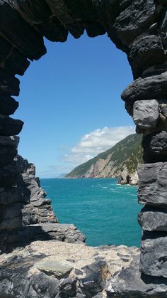 an open window in the side of a stone wall overlooking water and mountains with blue sky