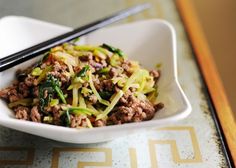 a white bowl filled with meat and veggies next to chopsticks on a table