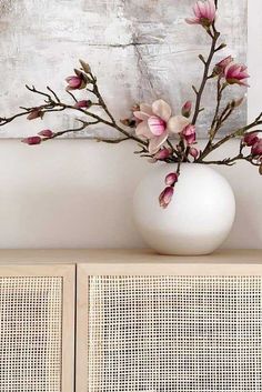 a vase filled with pink flowers sitting on top of a wooden table next to a painting