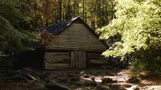 an old log cabin in the woods surrounded by rocks and trees with leaves around it