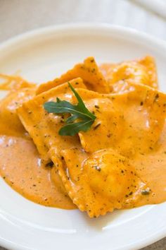 a white plate topped with ravioli covered in cheese sauce and garnished with parsley