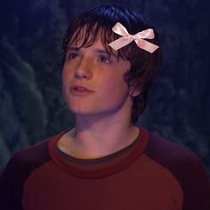 a young man with a pink bow on his head in front of a dark background