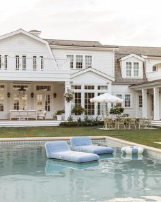 a large white house sitting next to a pool with chaise lounges on it