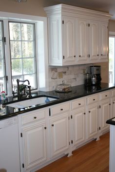 a large kitchen with white cabinets and black counter tops, along with hardwood floorsing