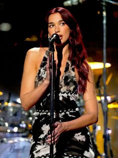 a woman with long red hair is singing into a microphone and wearing a floral dress