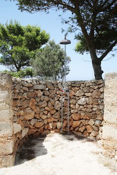 a stone wall with a lamp on top and trees in the backgroung