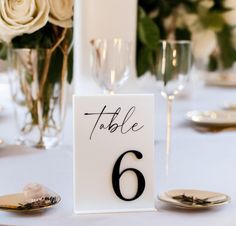 the table numbers are set up with gold plates and silver cutlery, as well as white roses