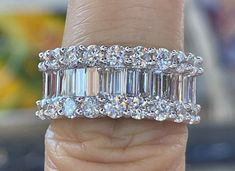 a woman's hand holding a ring with three baguets on it and two rows of diamonds in the middle