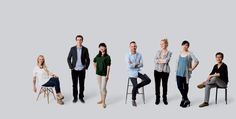 a group of people standing next to each other in front of a white background with one person sitting on a chair