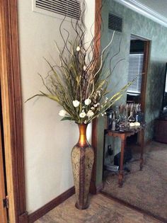 a tall vase with flowers in it sitting on the floor next to a mirror and table