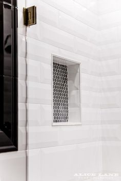 a bathroom with white tile and black accessories on the shower wall, along with a toilet paper dispenser