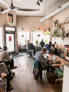 people sitting at tables in a restaurant with plants hanging from the ceiling and overhead fans