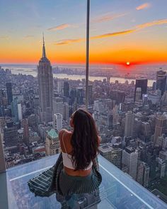 a woman sitting on top of a tall building looking at the city skyline in new york