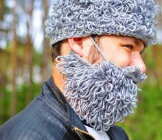 a man with a beard wearing a knitted hat in front of some trees and bushes