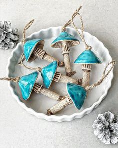 a white bowl filled with blue mushrooms on top of a table next to pine cones