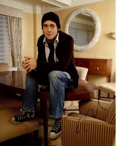 a man sitting on top of a wooden table in a living room next to a window