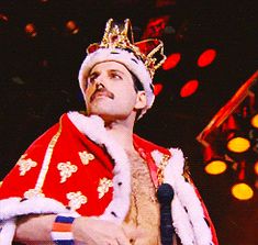 a man in a red and white costume with a crown on his head is speaking into a microphone